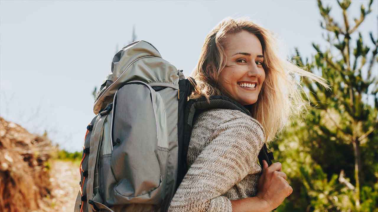 Testbild für KI-Bild Umfrage: ne lächelnde Frau mit Rucksack genießt eine Wanderung in der Natur an einem sonnigen Tag.