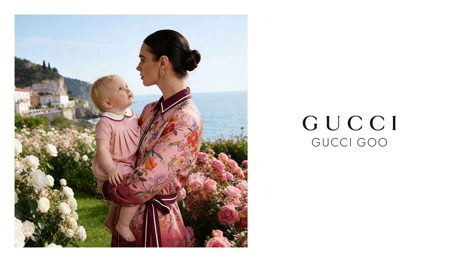 Mother holding a baby in a pink floral dress among roses by the sea; Gucci branding on the right side.